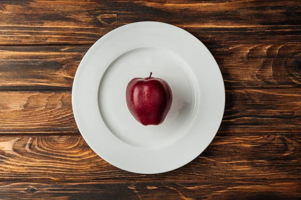 Ansicht des weißen Tellers mit rotem köstlichen Apfel auf Holztisch — Stockfoto