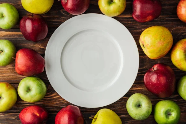 Draufsicht auf weißen Teller und reife bunte Äpfel auf Holztisch — Stockfoto