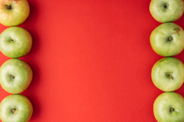 Vertikaler Rahmen reifer grüner Äpfel auf rotem Hintergrund — Stockfoto