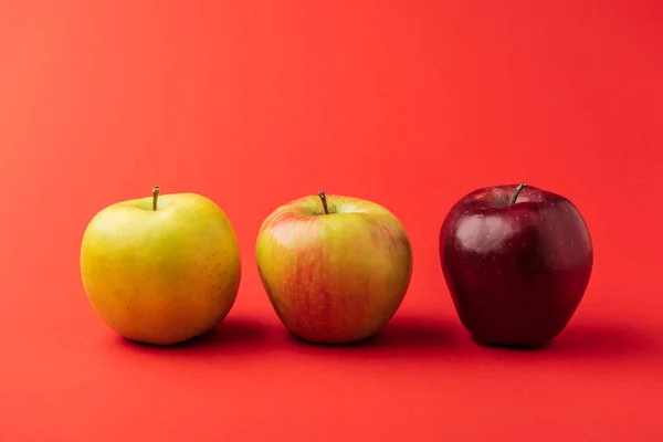 Linha de três maçãs maduras multicoloridas no fundo vermelho — Fotografia de Stock