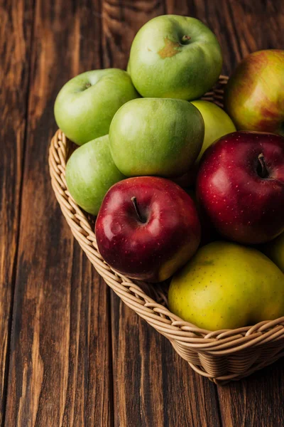 Panier en osier avec de savoureuses pommes multicolores sur table en bois — Photo de stock