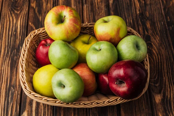 Wicker basket with ripe multicolored apples on rustic wooden table — Stock Photo