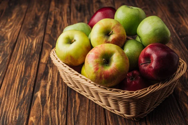 Ripe multicolored apples in wicker basket on rustic wooden table — Stock Photo