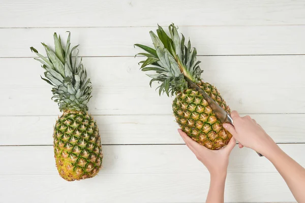 Cropped view of woman cutting ripe pineapple with knife — Stock Photo