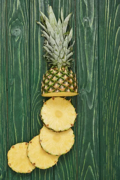 Vista superior de los círculos cortados en rodajas de sabrosa piña en la mesa de madera verde - foto de stock