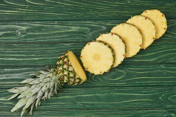 Draufsicht auf geschnittene Kreise gelber reifer Ananas auf grünem Holztisch — Stockfoto