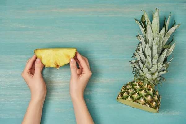 Cropped view of woman holding slice of pineapple on turquoise wooden table — Stock Photo