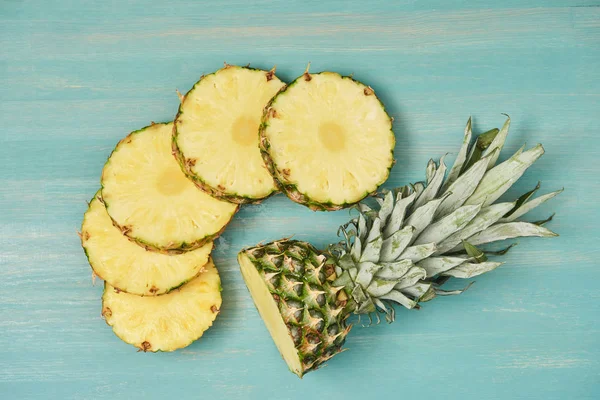 Top view of sliced pineapple circles near cut pineapple on turquoise wooden table — Stock Photo