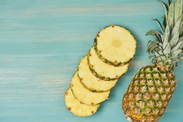 Draufsicht auf geschnittene saftige Kreise in der Nähe ganzer Ananas auf türkisfarbenem Holztisch — Stockfoto