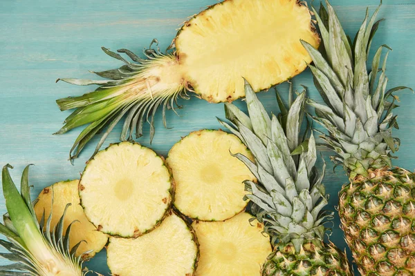 Vue de dessus d'ananas entiers et tranchés sur table en bois turquoise — Photo de stock