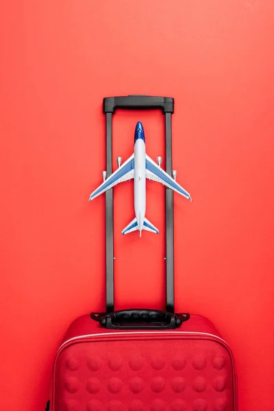 Vista superior de la bolsa de viaje con asa y avión de juguete sobre fondo rojo - foto de stock