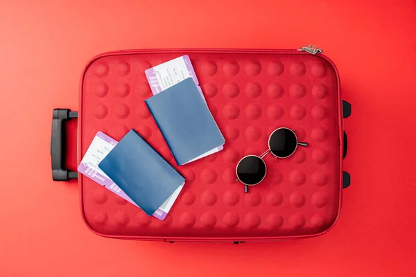 Вид зверху на туристичну сумку, паспорти, авіаквитки та сонцезахисні окуляри на червоному тлі — стокове фото