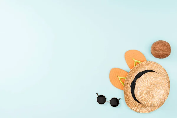 Vista superior de óculos de sol, chinelos, chapéu de palha e coco no fundo azul — Fotografia de Stock