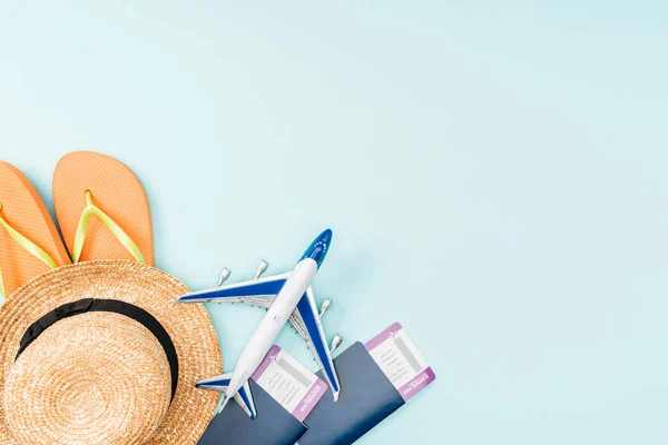 Vista superior de pasaportes, billetes de avión, sombrero de paja, chanclas y avión de juguete sobre fondo azul - foto de stock