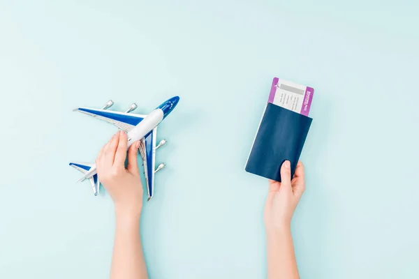 Cropped view of woman holding passport, air ticket and toy plane on blue background — Stock Photo