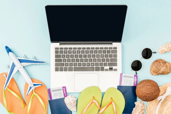 Top view of laptop with blank screen, flip flops, passports with air tickets, sunglasses, seashells, straw hat and plane toy on blue background — Stock Photo