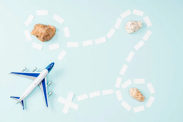Top view of toy plane, dotted line and seashells on blue background — Stock Photo