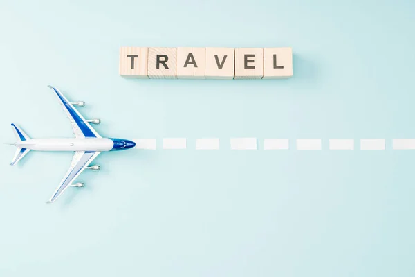 Draufsicht auf Spielzeugflugzeug, gestrichelte Linie und Holzwürfel mit Reiseschrift auf blauem Hintergrund — Stockfoto