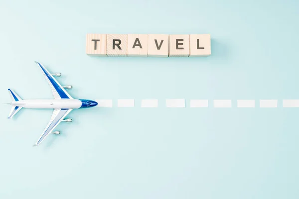 Vista superior del avión de juguete, línea de puntos y cubos de madera con letras de viaje sobre fondo azul - foto de stock