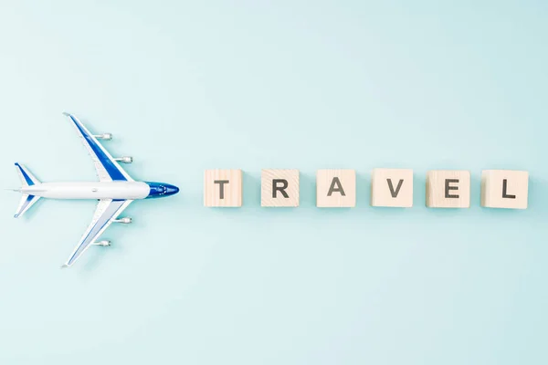 Vista superior del avión de juguete y cubos de madera con letras de viaje sobre fondo azul - foto de stock