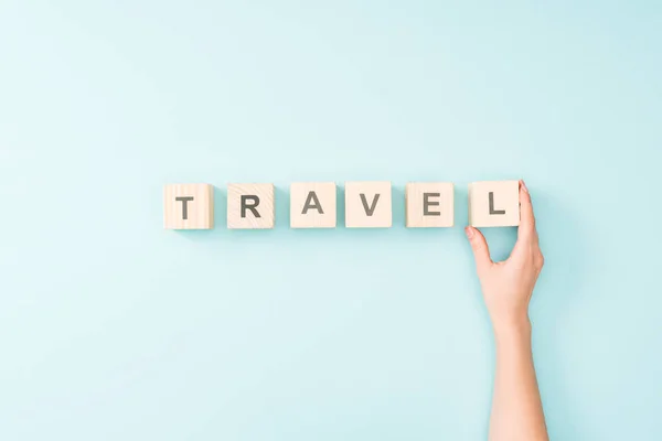 Cropped view of woman and wooden cubes with travel lettering on blue background — Stock Photo