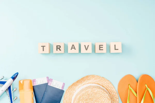 Top view of wooden cubes with travel lettering, straw hat, flip flops, passports and air tickets on blue background — Stock Photo