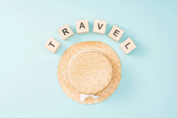 Vista dall'alto di cubi in legno con scritte da viaggio e cappello di paglia su sfondo blu — Foto stock