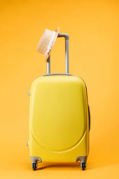 Travel bag with wheels and straw hat on yellow background — Stock Photo