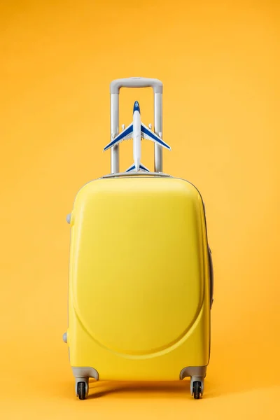 Bolsa de viaje con ruedas y avión de juguete sobre fondo amarillo - foto de stock