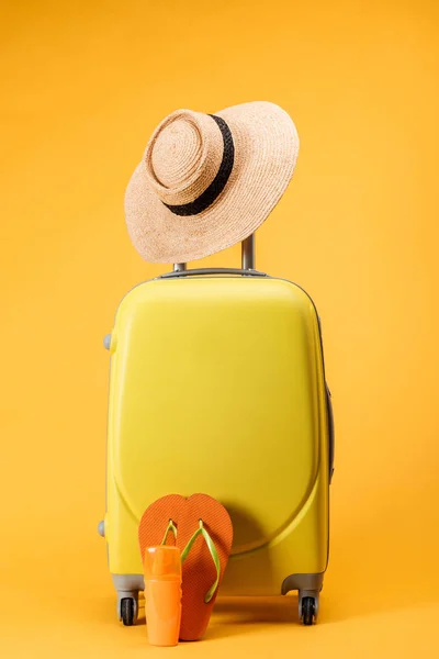 Travel bag with wheels, straw hat and flip flops on yellow background — Stock Photo