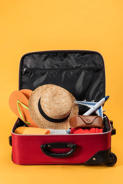 Avión de juguete, sombrero de paja, chanclas y ropa en bolsa de viaje sobre fondo amarillo - foto de stock