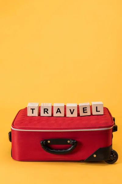 Bolsa de viaje y cubos de madera con letras de viaje sobre fondo amarillo - foto de stock