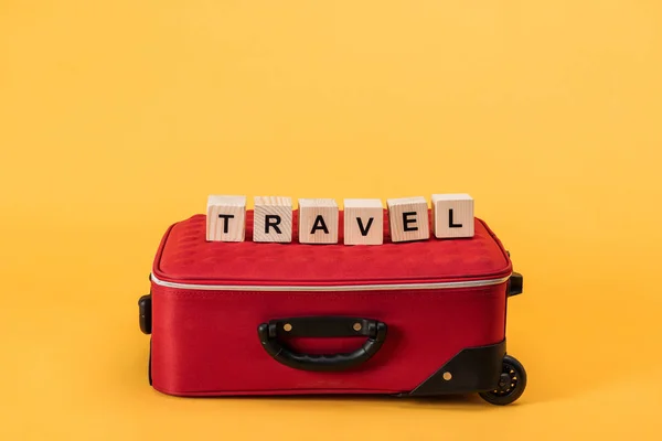 Bolsa de viaje con ruedas y cubos de madera con letras de viaje sobre fondo amarillo - foto de stock