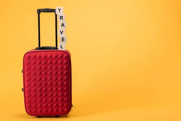 Reisetasche mit Rädern und Holzwürfeln mit Reiseaufschrift auf gelbem Hintergrund — Stockfoto