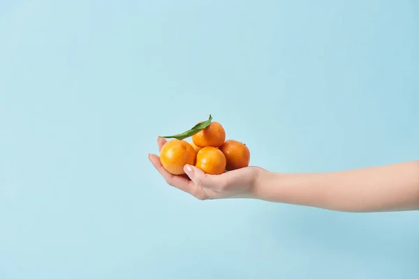 Vista recortada de la mujer sosteniendo mandarinas orgánicas en la mano aislado en azul - foto de stock