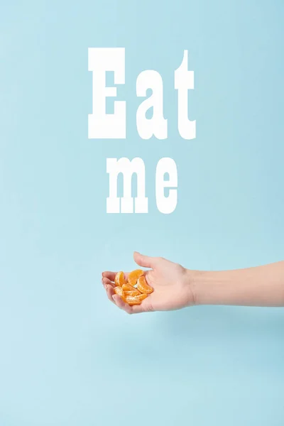 Vue recadrée de femme tenant des tranches de mandarine pelée près de me manger lettrage isolé sur bleu — Photo de stock
