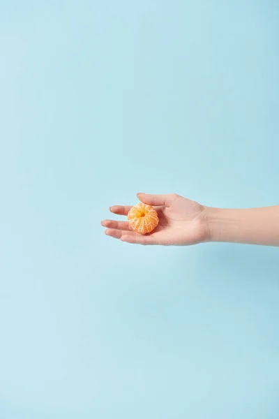 Vista recortada de la mujer sosteniendo mandarina pelada en la mano aislada en azul - foto de stock