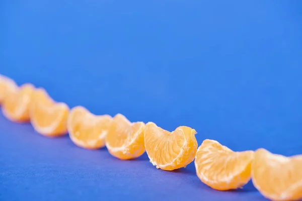 Enfoque selectivo de rodajas de mandarina peladas sobre fondo azul - foto de stock
