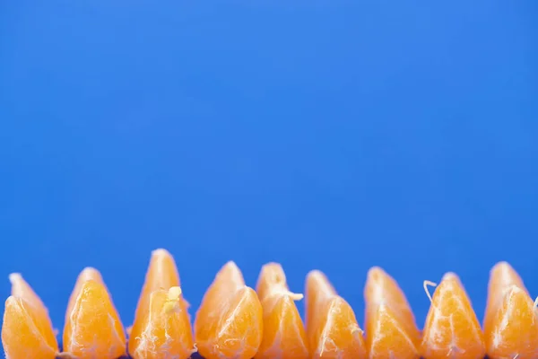 Enfoque selectivo de rebanadas de mandarina peladas orgánicas aisladas en azul - foto de stock