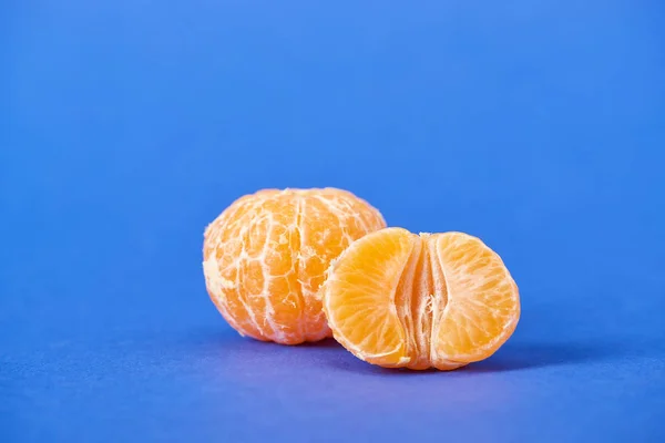 Half of peeled tangerine near whole clementine on blue background — Stock Photo