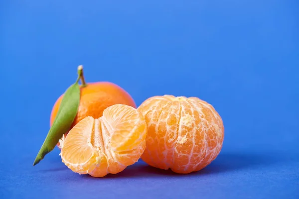 Metà del mandarino pelato vicino a clementine intere su fondo blu — Foto stock