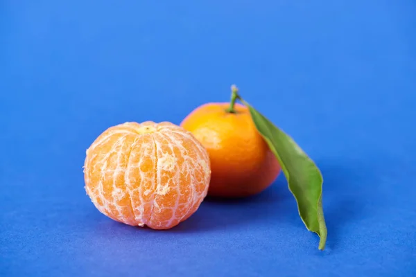 Очищенный органический мандарин рядом с клементиной с изюминкой на синем фоне — стоковое фото