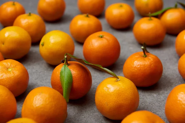 Selective focus of organic orange tangerines with green leaves on grey table — Stock Photo