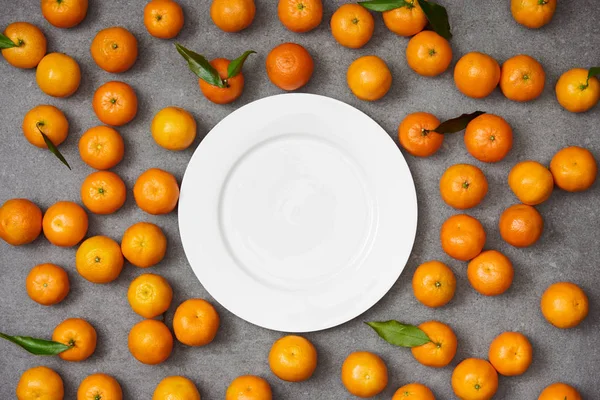 Top view of sweet organic tangerines near white plate on grey table — Stock Photo