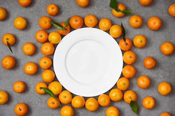 Top view of fresh organic tangerines near white plate on grey table — Stock Photo