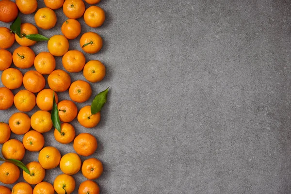 Top view of ripe organic clementines with green leaves on grey table — Stock Photo