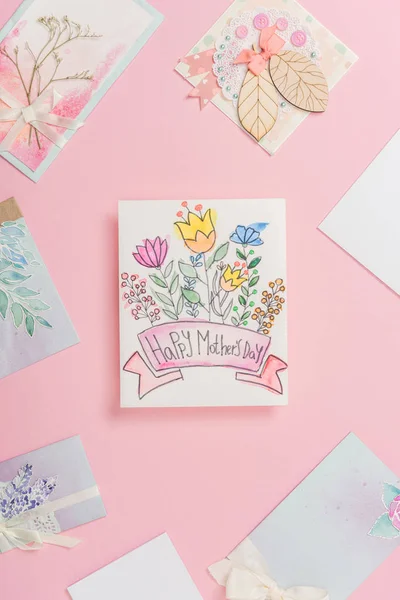 Joyeuse carte de vœux de la fête des mères avec des fleurs, et différentes cartes postales de la fête des mères disposées autour sur fond rose — Photo de stock
