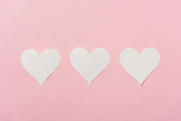 Coeurs en papier blanc disposés en rangée sur fond rose — Photo de stock