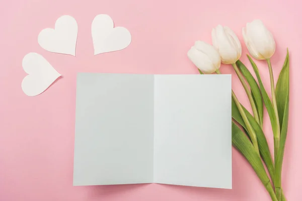 Blank greeting card, white paper hearts and white tulips on pink background — Stock Photo