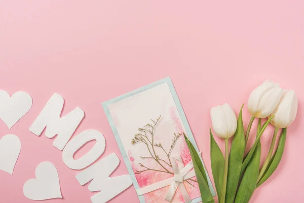 Tarjetas postales del día de las madres decoradas con plantas secas y arco, tulipanes blancos, corazones de papel y la palabra mamá sobre fondo rosa - foto de stock